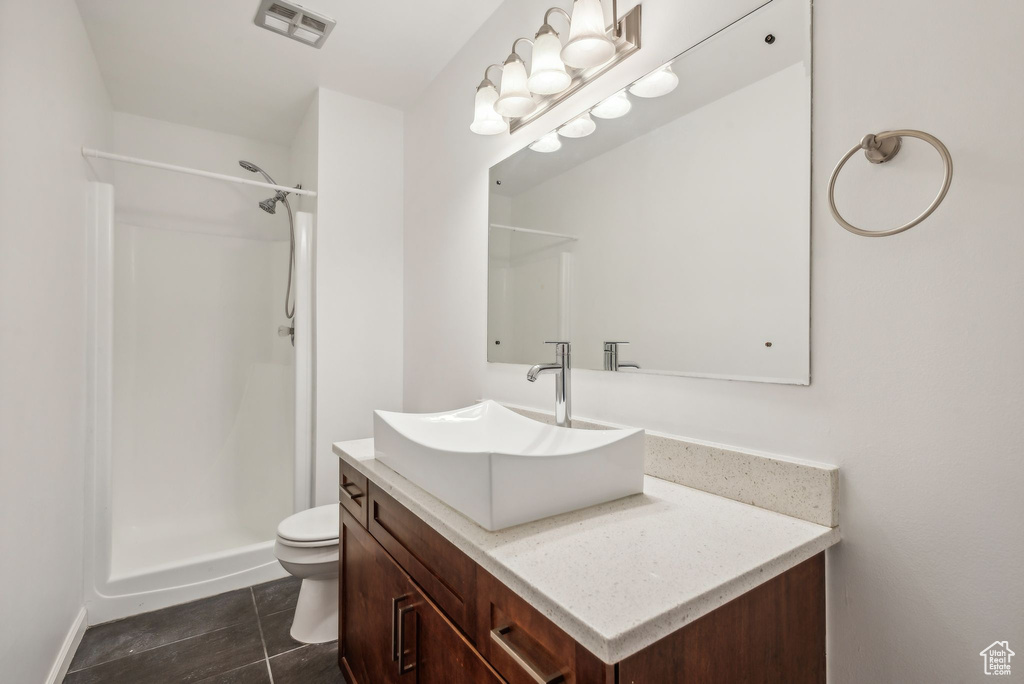 Bathroom with vanity, a shower, toilet, and tile patterned flooring