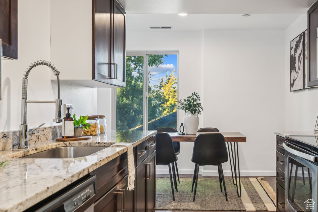 Kitchen featuring dark brown cabinetry, light stone countertops, sink, and stainless steel appliances