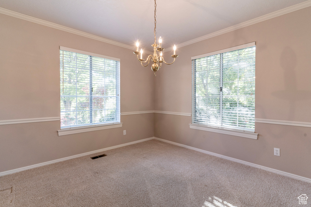 Carpeted empty room featuring plenty of natural light, ornamental molding, and a notable chandelier