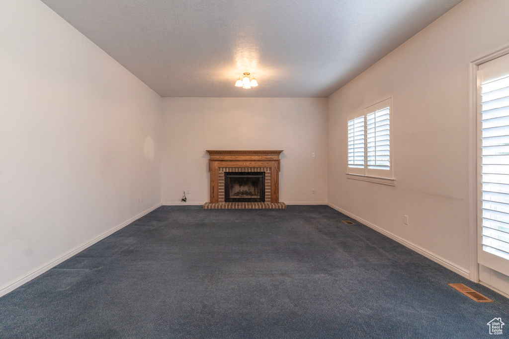 Unfurnished living room featuring dark carpet, a fireplace, and plenty of natural light