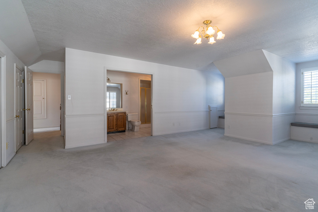 Additional living space with light colored carpet, a notable chandelier, and a textured ceiling