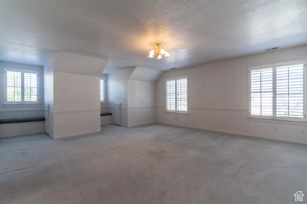 Additional living space with light carpet, a healthy amount of sunlight, and a textured ceiling