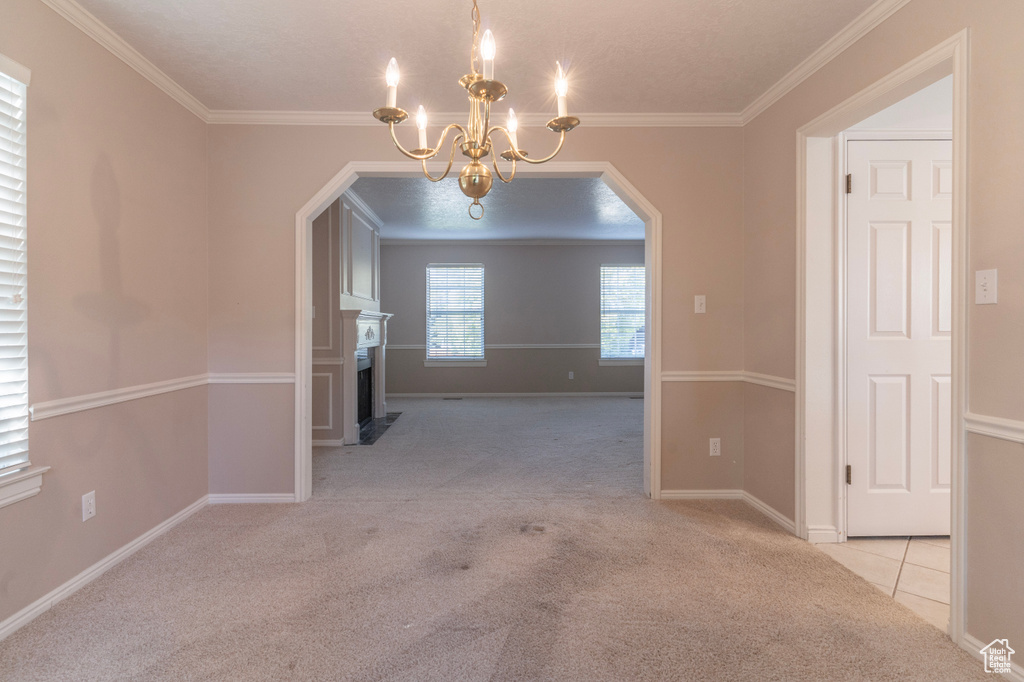 Unfurnished dining area featuring crown molding, light colored carpet, and a notable chandelier