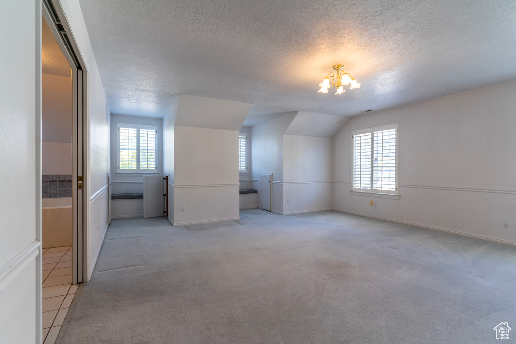 Bonus room with lofted ceiling, plenty of natural light, light colored carpet, and a textured ceiling