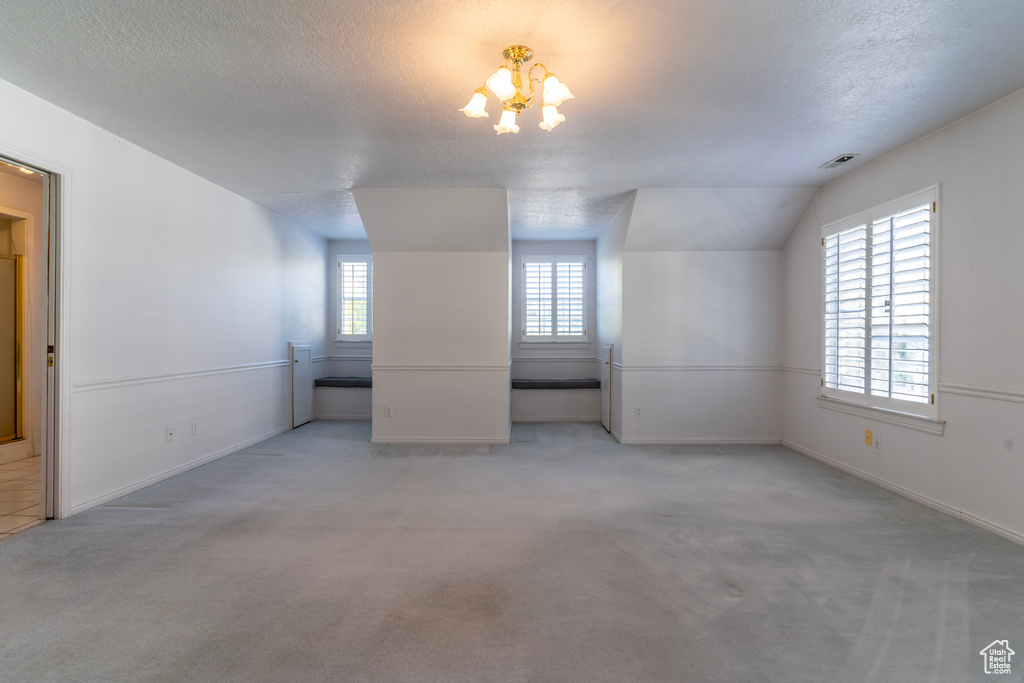 Carpeted spare room with vaulted ceiling, an inviting chandelier, a wealth of natural light, and a textured ceiling