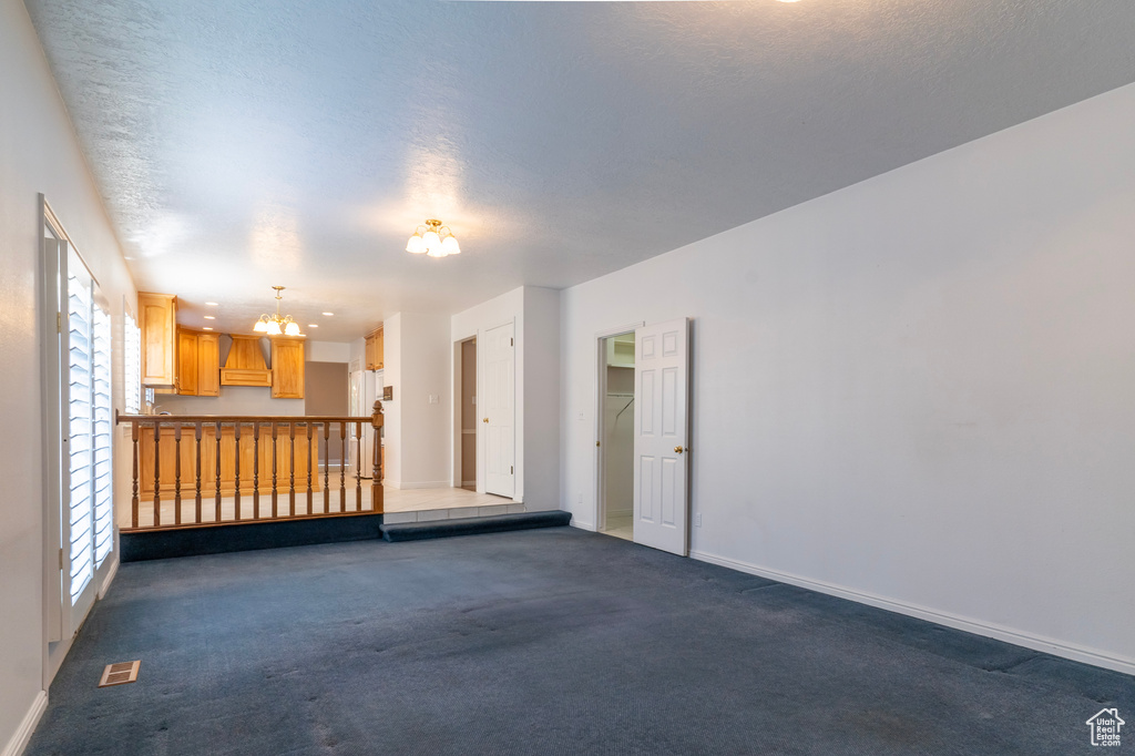 Spare room featuring a notable chandelier, dark carpet, and a textured ceiling