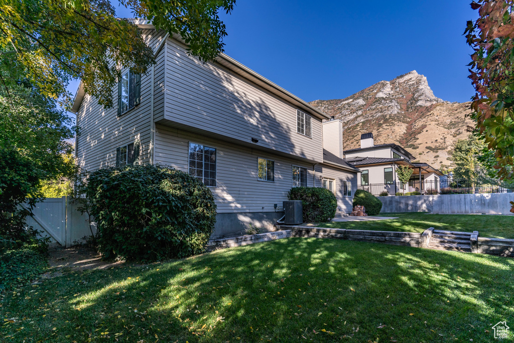 Back of property featuring a mountain view, a lawn, and central AC