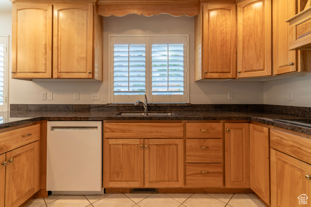 Kitchen with dark stone countertops, light tile patterned floors, dishwasher, and sink