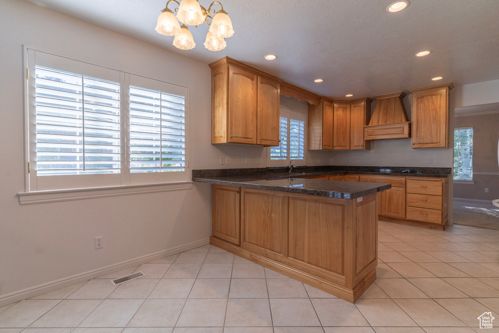 Kitchen featuring kitchen peninsula, a notable chandelier, custom exhaust hood, decorative light fixtures, and light tile patterned floors