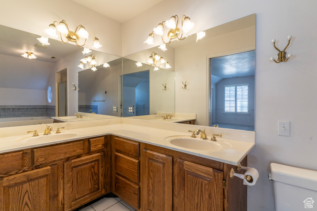 Bathroom with toilet, vaulted ceiling, tile patterned floors, a bathing tub, and vanity