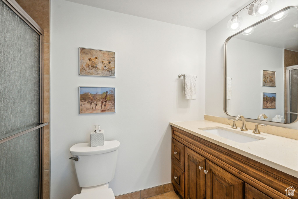 Bathroom with toilet, a shower with shower door, vanity, and tile patterned floors