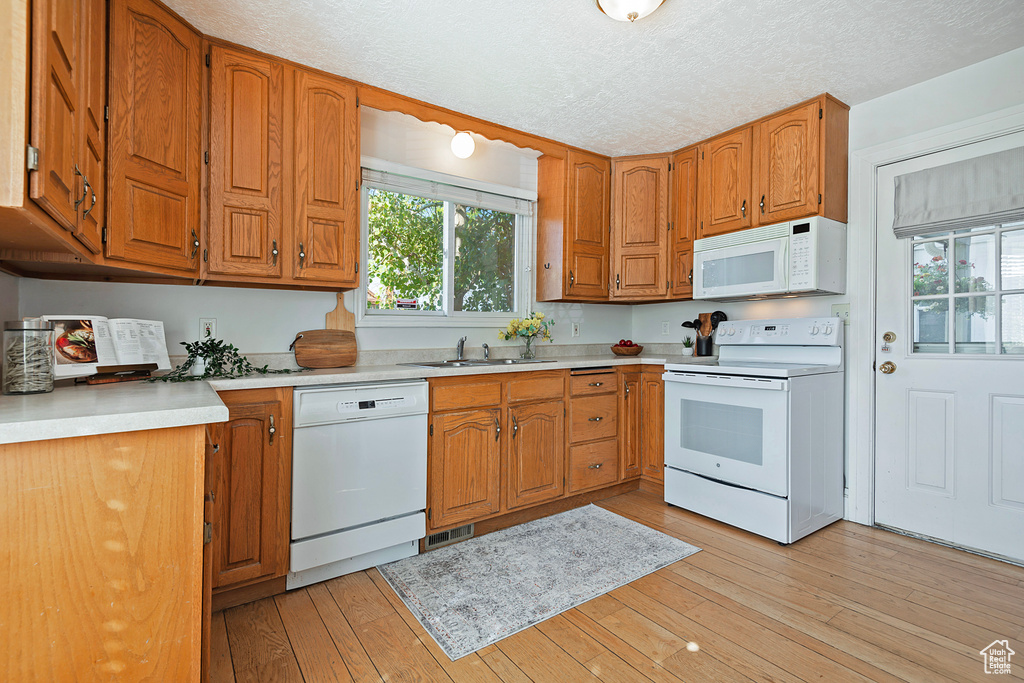 Kitchen featuring white appliances, a textured ceiling, sink, and light wood-type flooring