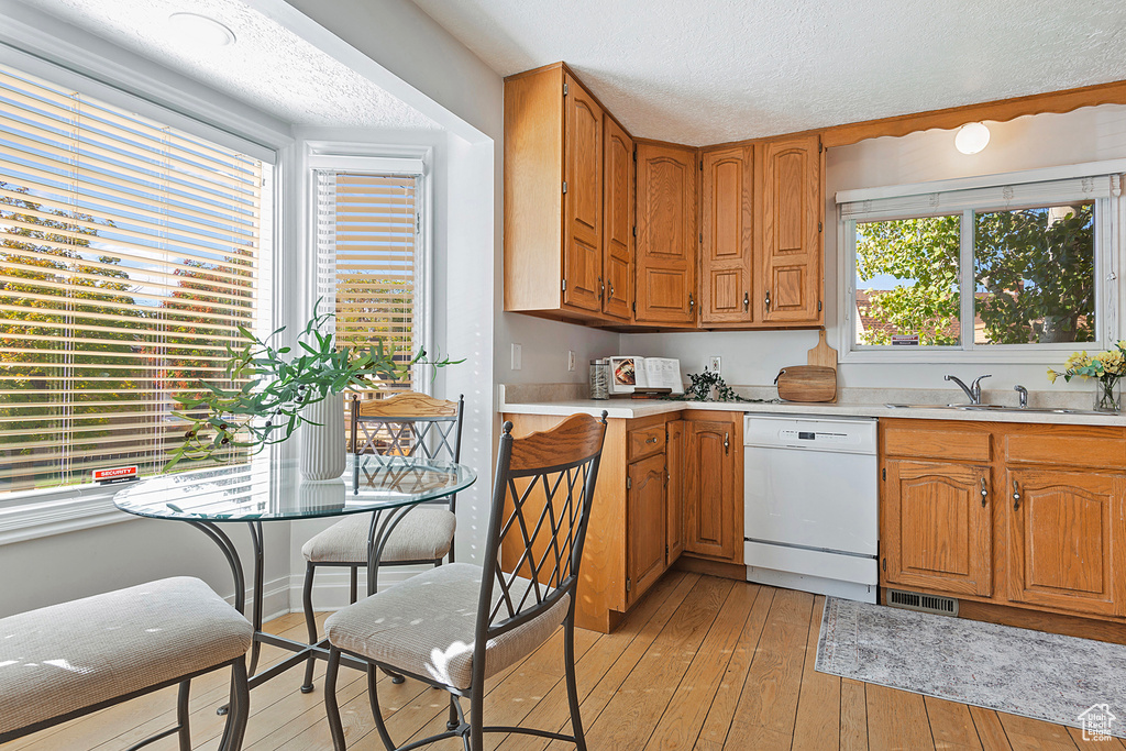 Kitchen with white dishwasher, sink, light hardwood / wood-style flooring, and a textured ceiling