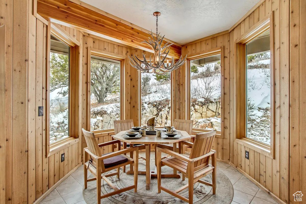 Dining area with an inviting chandelier, light tile patterned flooring, a healthy amount of sunlight, and wood walls