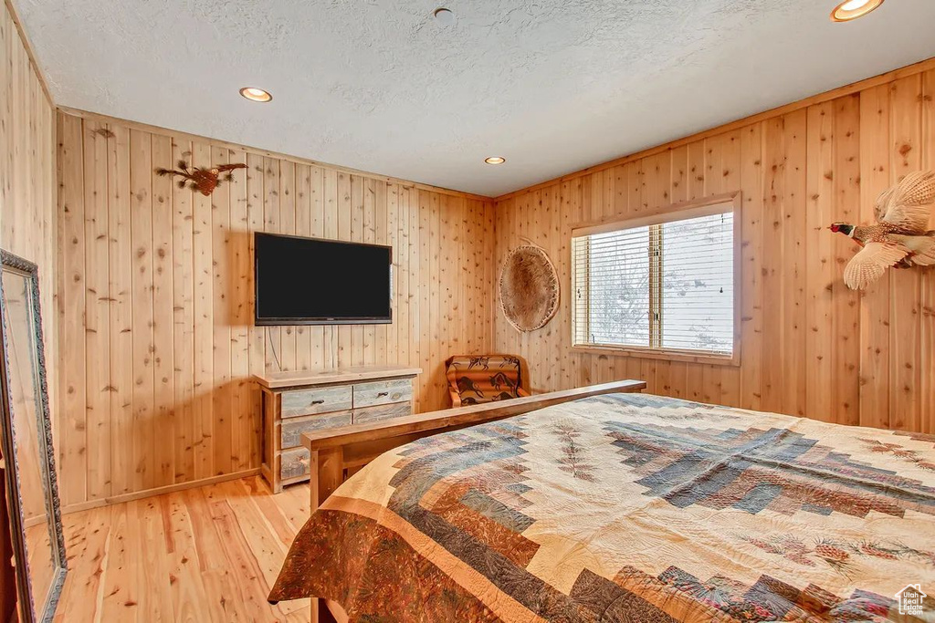 Bedroom featuring light hardwood / wood-style floors, wood walls, and a textured ceiling