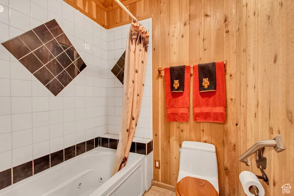 Bathroom with wooden walls, shower / tub combo with curtain, and toilet