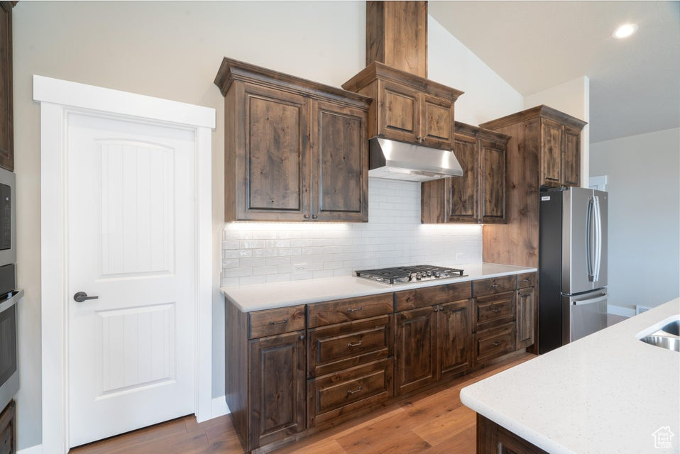 Kitchen with stainless steel appliances, dark wood-type flooring, vaulted ceiling, and backsplash