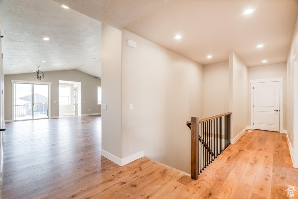 Corridor featuring light hardwood / wood-style floors, a textured ceiling, and vaulted ceiling