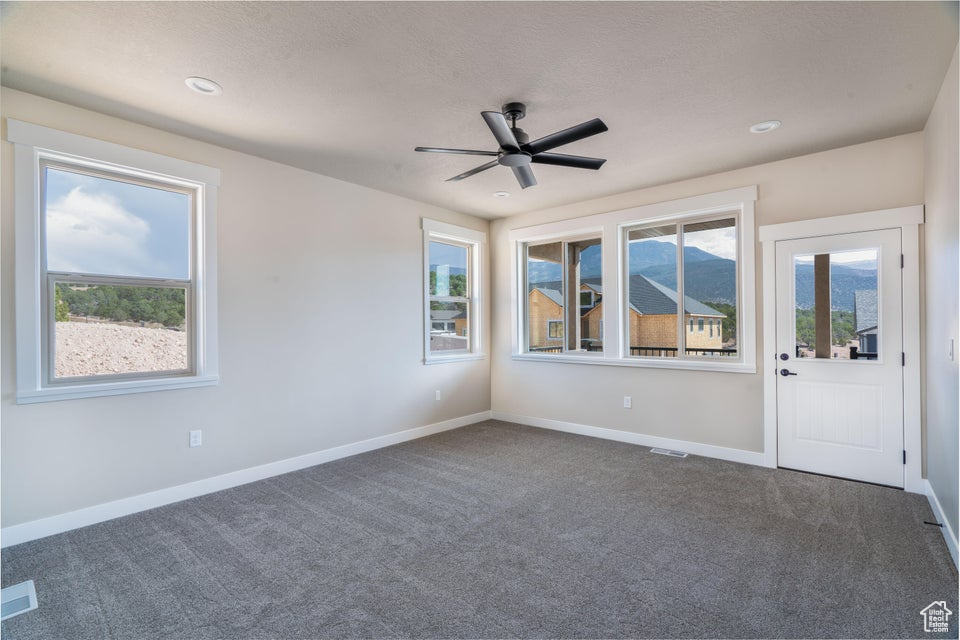 Empty room featuring dark colored carpet and ceiling fan