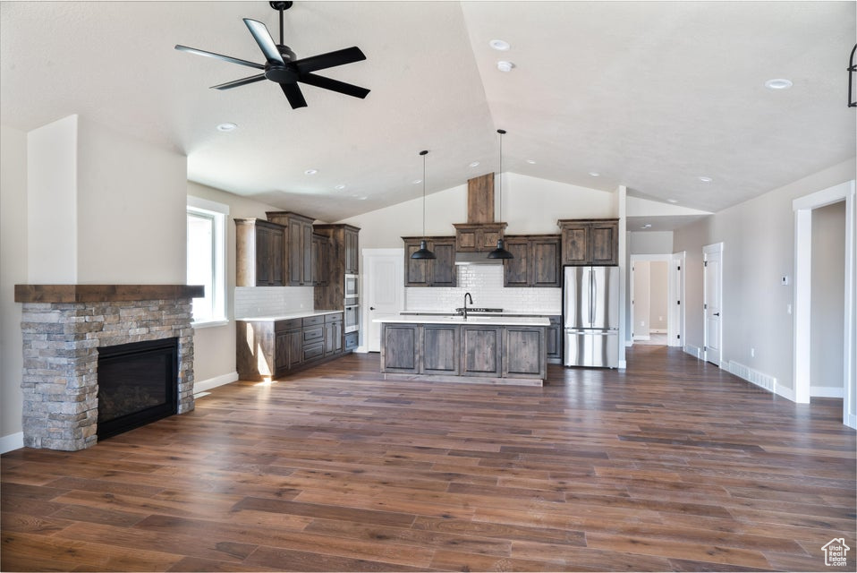 Unfurnished living room with sink, a stone fireplace, dark hardwood / wood-style flooring, ceiling fan, and lofted ceiling