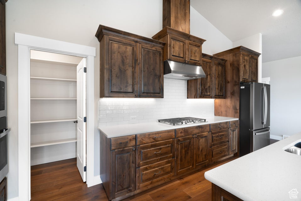 Kitchen featuring backsplash, dark hardwood / wood-style flooring, vaulted ceiling, dark brown cabinetry, and stainless steel appliances