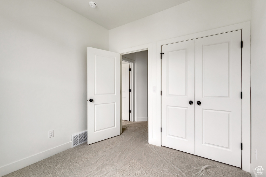 Unfurnished bedroom featuring a closet, visible vents, light colored carpet, and baseboards