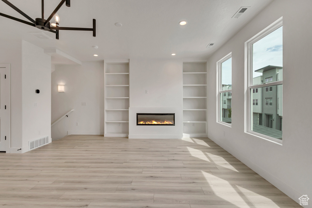 Unfurnished living room featuring a glass covered fireplace, visible vents, light wood-style floors, and recessed lighting