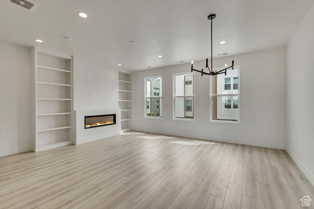 Unfurnished living room featuring visible vents, light wood-style floors, baseboards, a notable chandelier, and built in shelves
