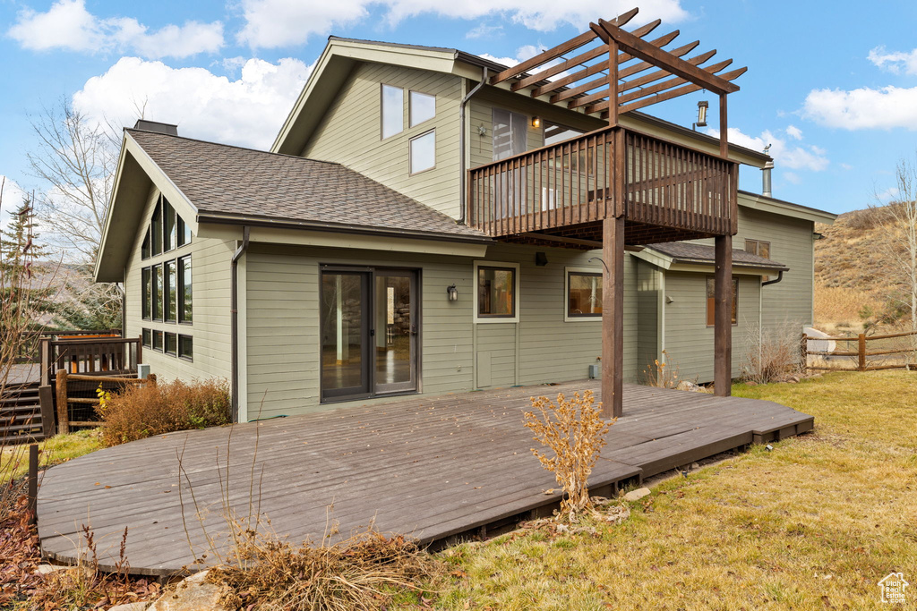 Rear view of house featuring a pergola, a deck, and a lawn