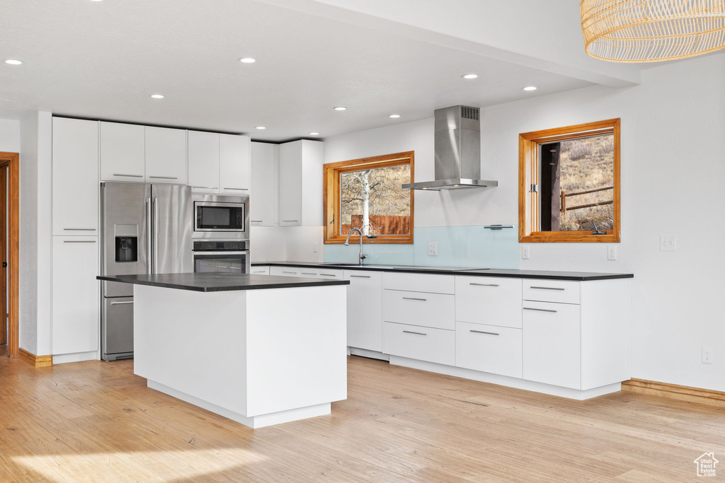 Kitchen featuring white cabinets, stainless steel appliances, wall chimney range hood, and a center island