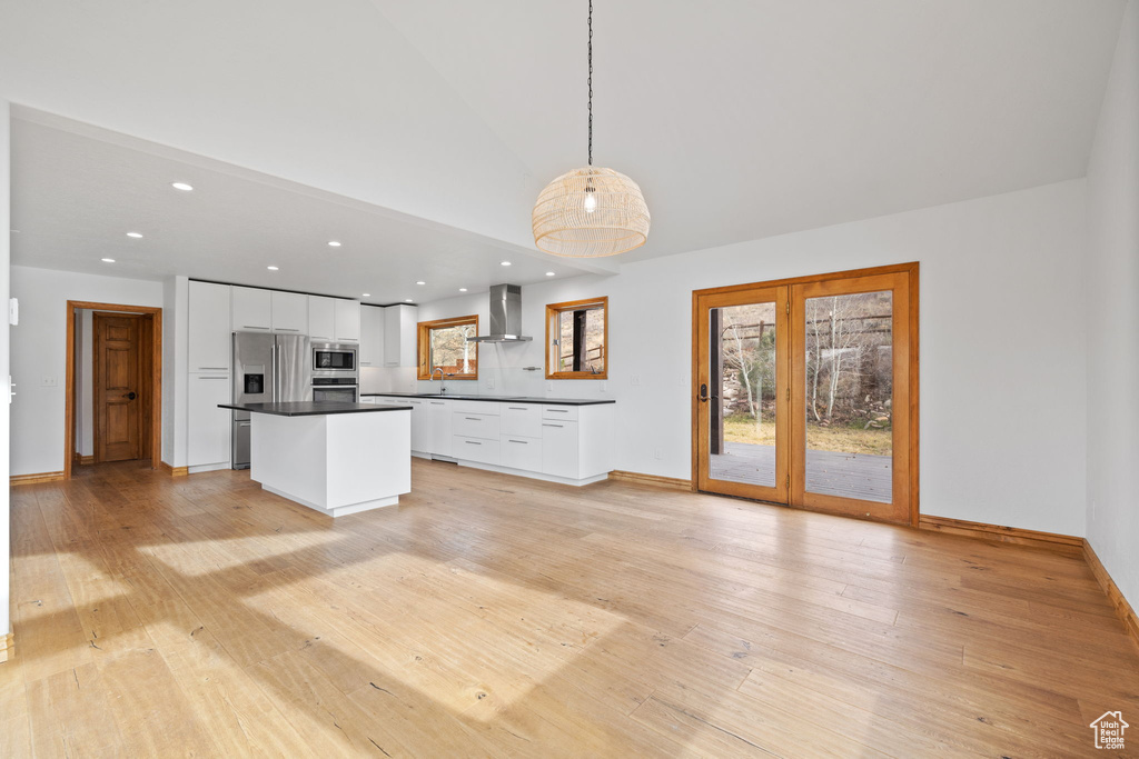 Kitchen with appliances with stainless steel finishes, pendant lighting, wall chimney range hood, and white cabinetry