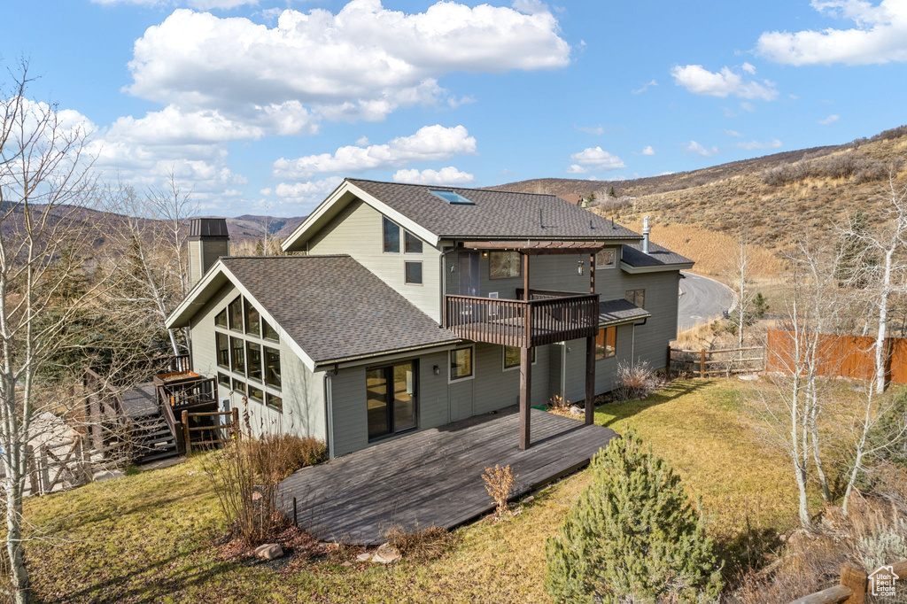 Rear view of property with a deck with mountain view and a lawn