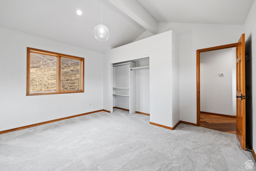 Unfurnished bedroom with lofted ceiling with beams, a closet, and light colored carpet