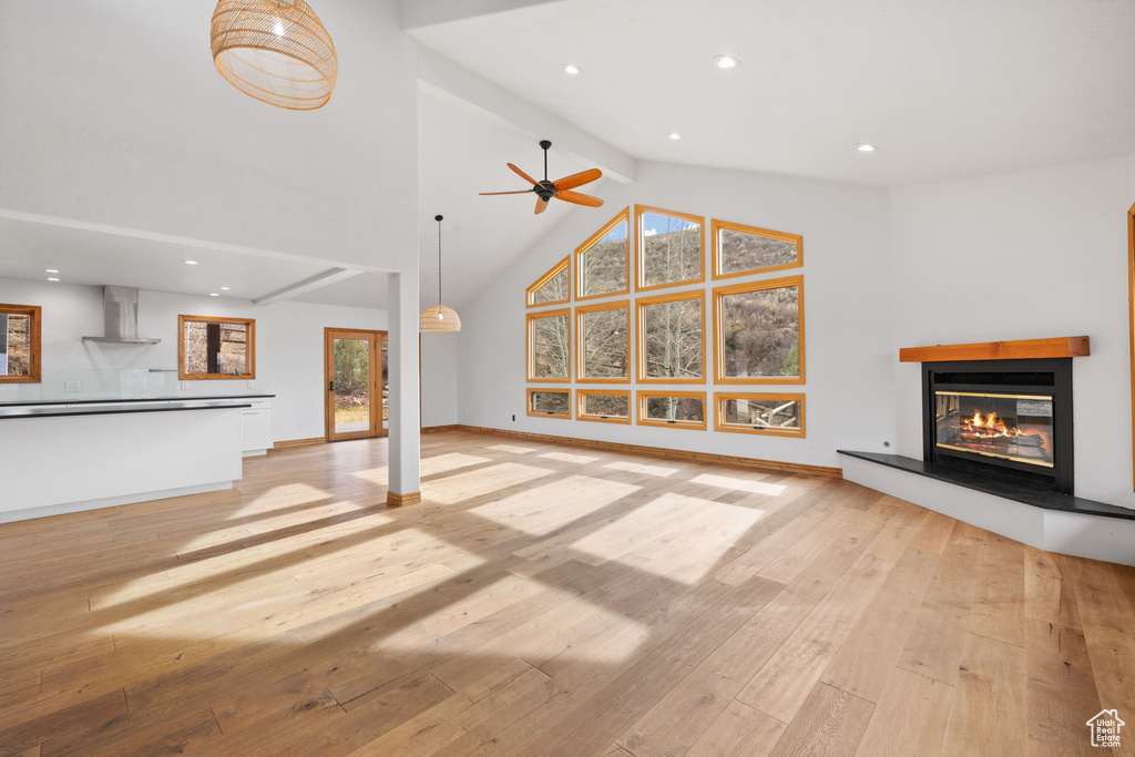 Unfurnished living room featuring ceiling fan, beam ceiling, light hardwood / wood-style floors, and high vaulted ceiling