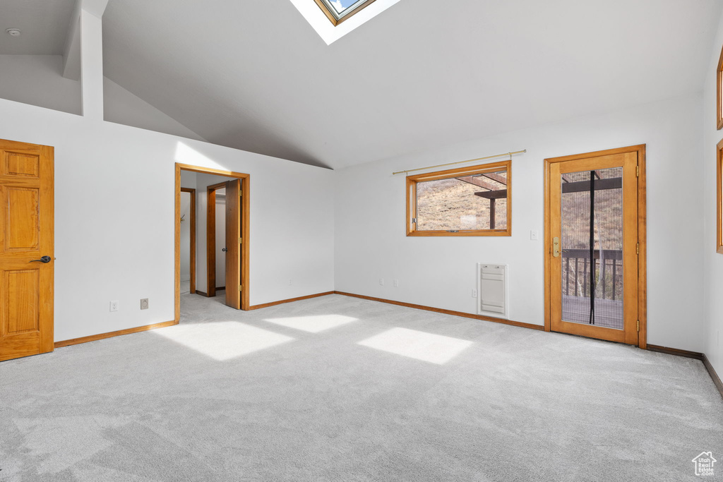 Empty room with a skylight, light colored carpet, beam ceiling, heating unit, and high vaulted ceiling