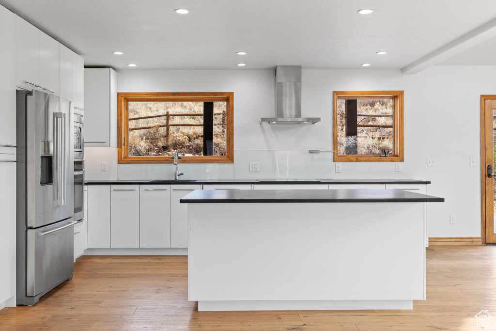 Kitchen featuring stainless steel appliances, sink, wall chimney range hood, and white cabinetry