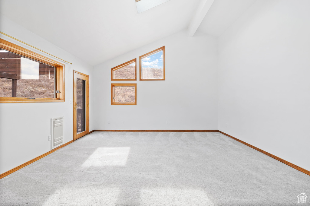 Unfurnished room featuring vaulted ceiling with skylight and light carpet