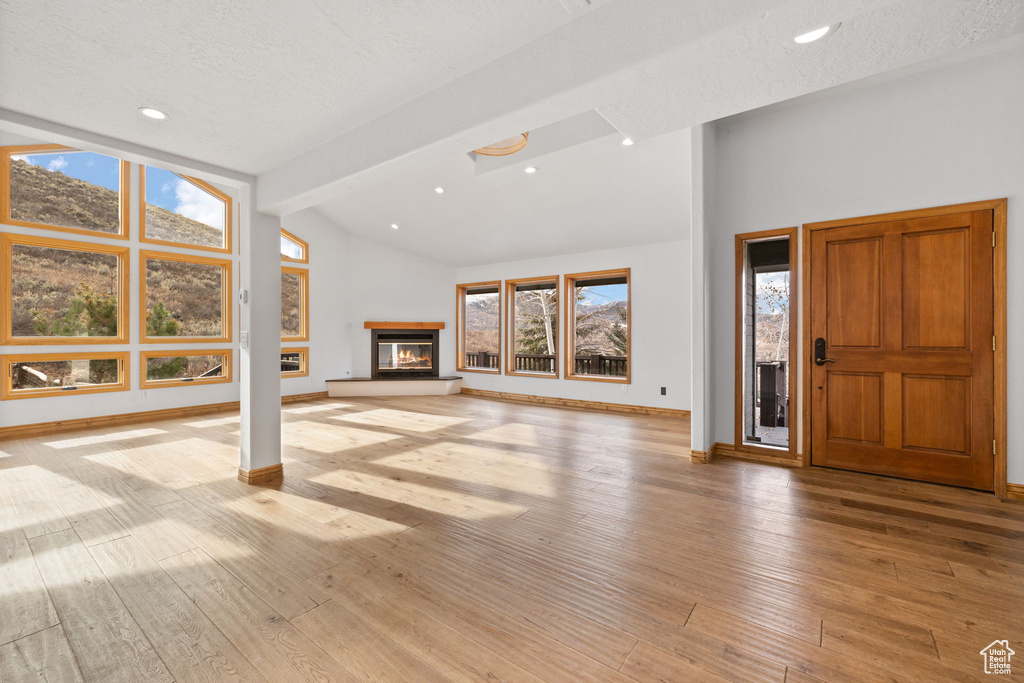 Unfurnished living room with beamed ceiling, light wood-type flooring, and a textured ceiling