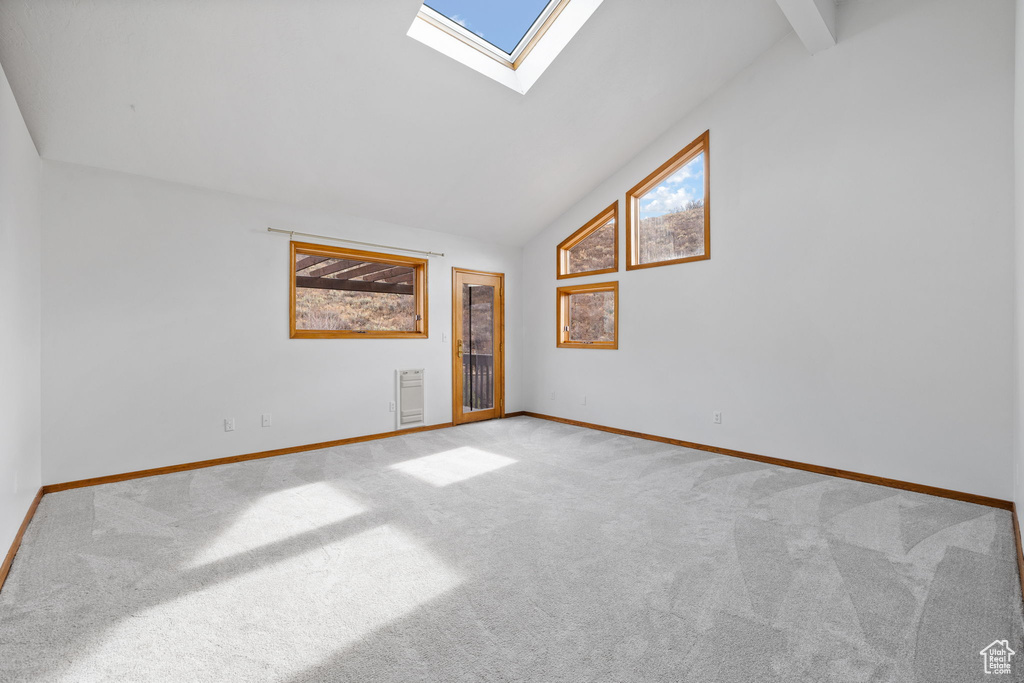 Spare room with a skylight, high vaulted ceiling, and light carpet