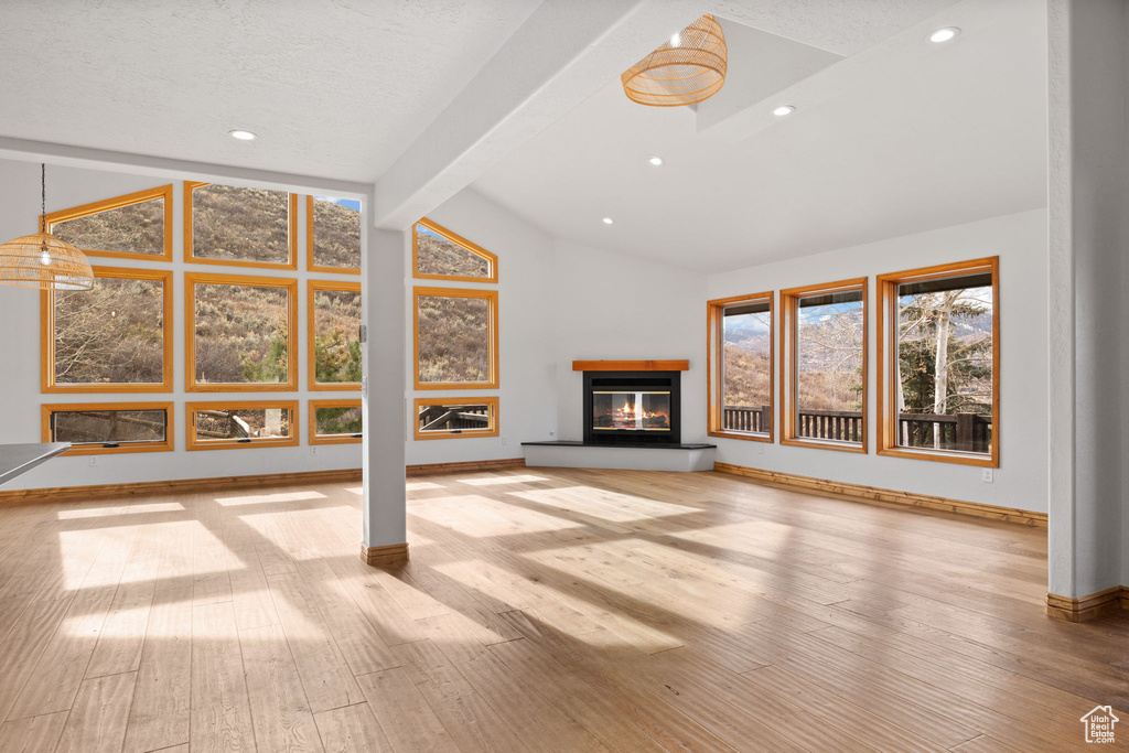 Unfurnished living room featuring light hardwood / wood-style floors, vaulted ceiling with beams, and a textured ceiling