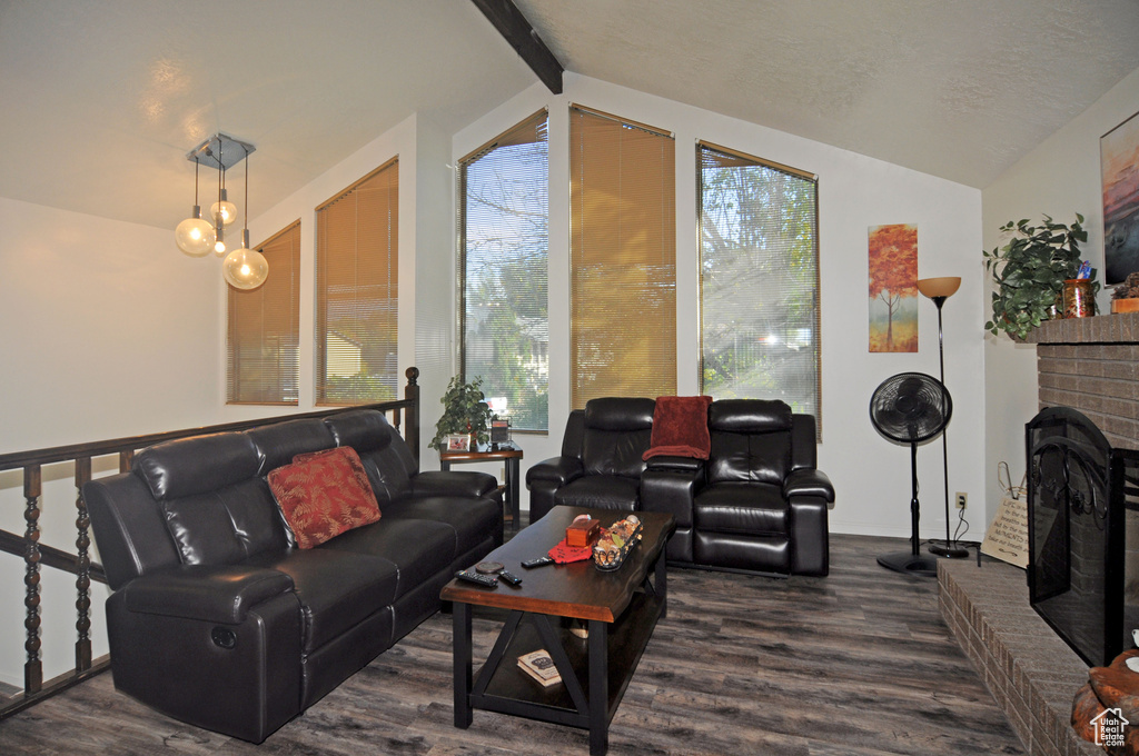 Living room with dark hardwood / wood-style floors, lofted ceiling with beams, and a fireplace