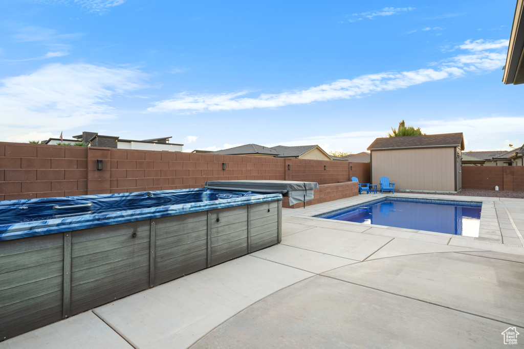 View of swimming pool with a patio area, a shed, and a hot tub