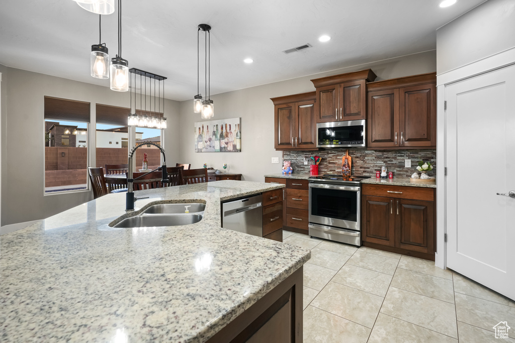 Kitchen featuring stainless steel appliances, light stone countertops, sink, and decorative light fixtures