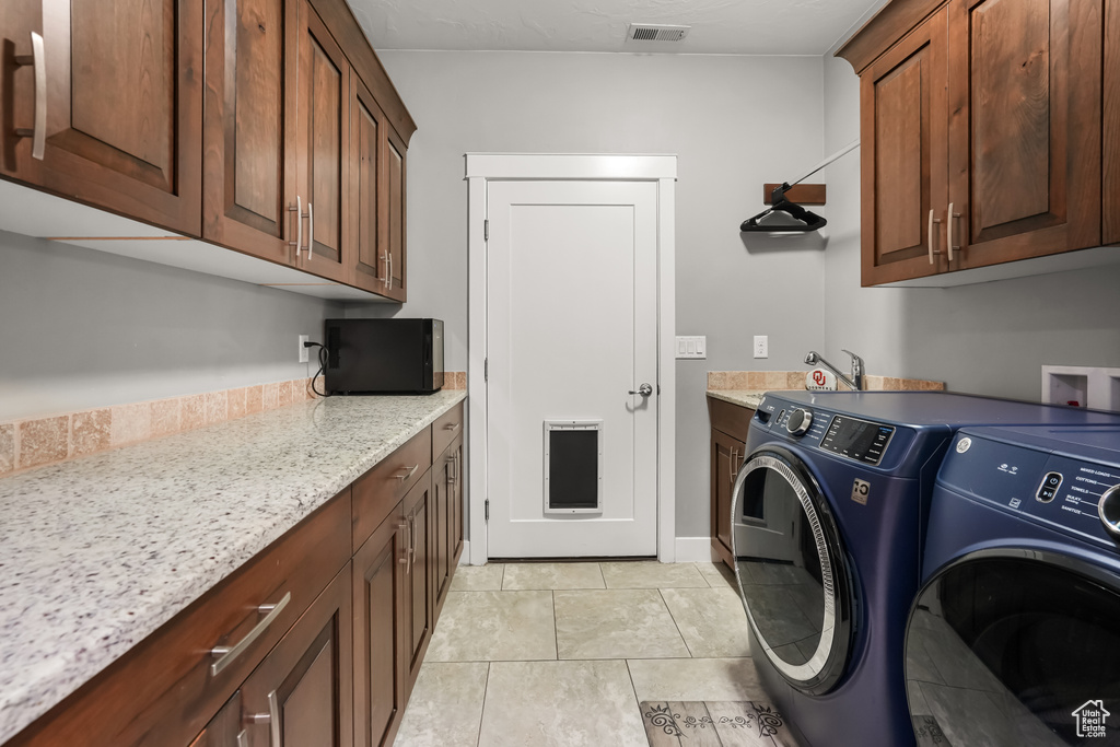 Laundry area with sink, washer and clothes dryer, cabinets, and light tile patterned flooring