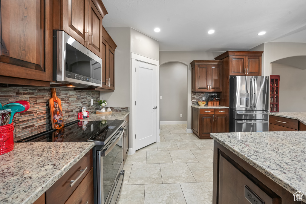 Kitchen featuring light stone counters, appliances with stainless steel finishes, light tile patterned floors, and decorative backsplash