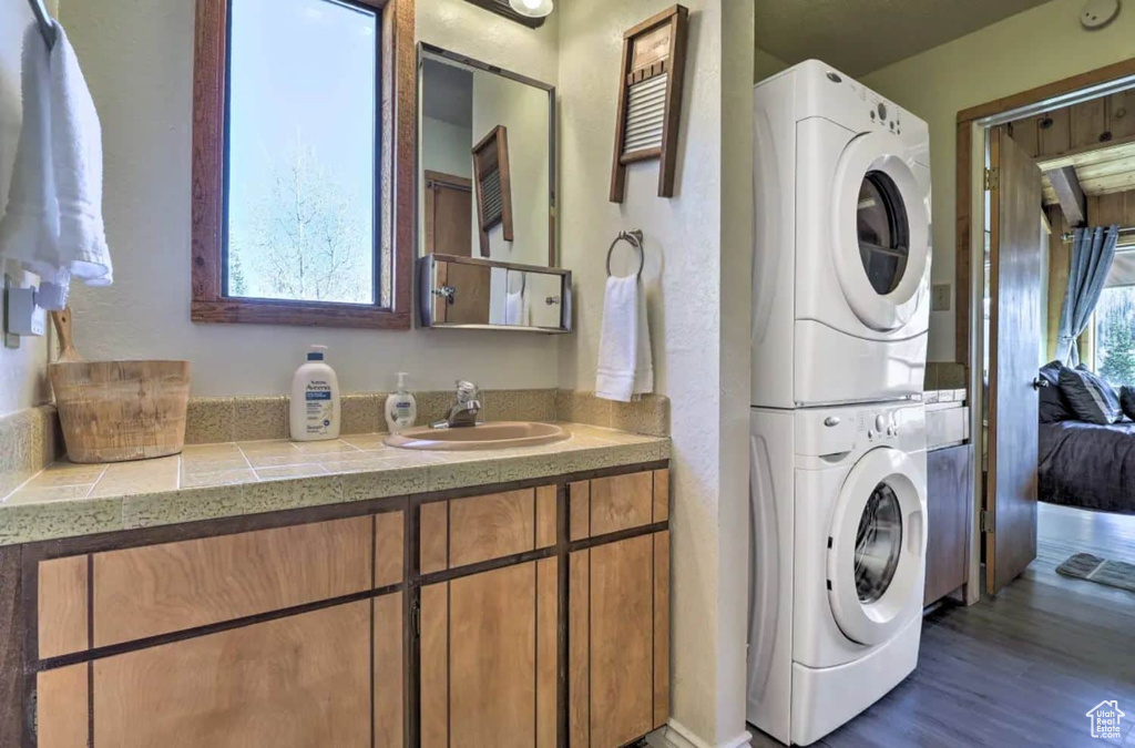 Laundry room with dark wood-type flooring, sink, and stacked washer / drying machine