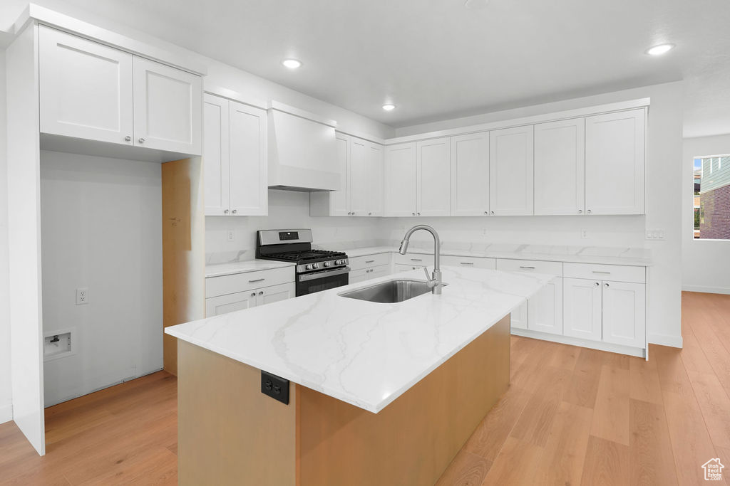 Kitchen featuring an island with sink, gas range, white cabinets, and sink