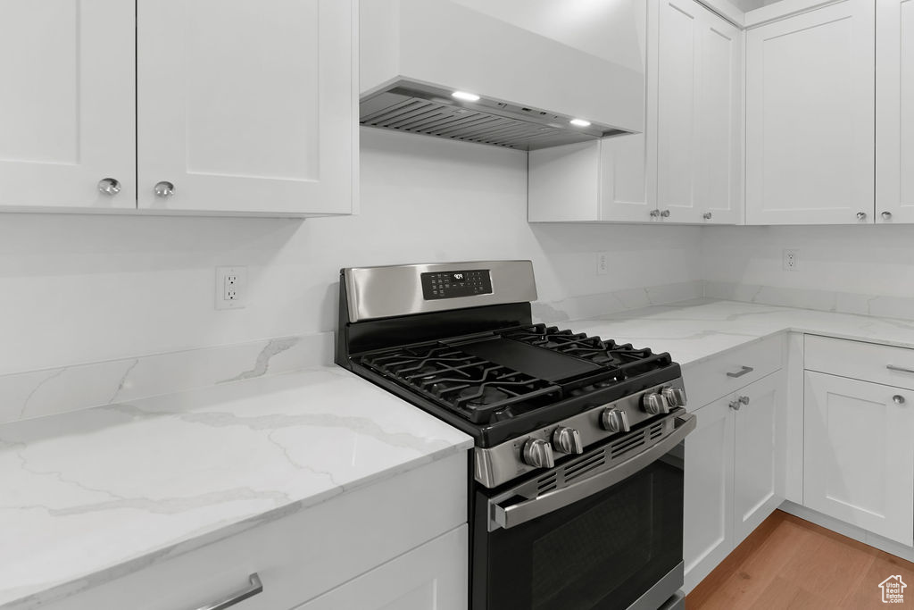 Kitchen featuring white cabinets, premium range hood, light hardwood / wood-style flooring, and stainless steel range with gas stovetop