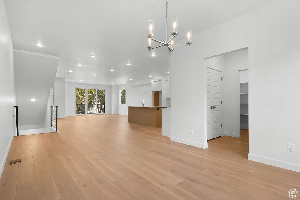 Unfurnished living room featuring an inviting chandelier, light wood-type flooring, and sink