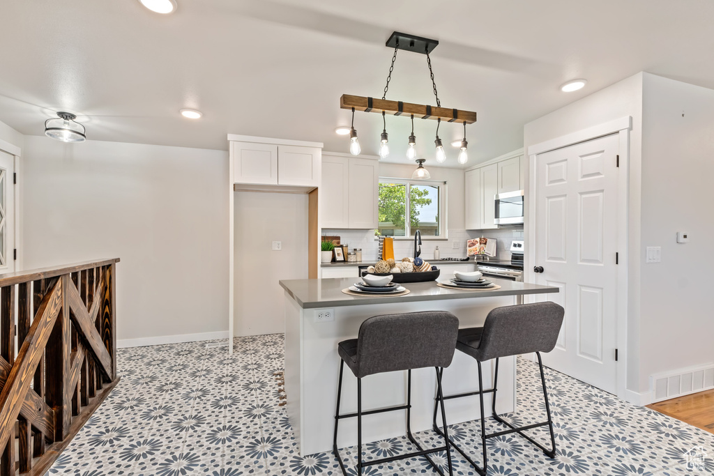 Kitchen with hanging light fixtures, white cabinetry, a kitchen bar, sink, and white range